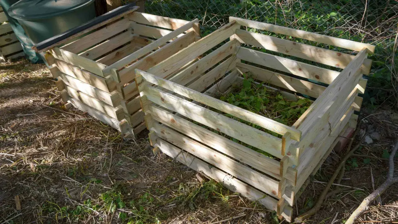 Deux composteurs maison en bois, l'un rempli de verdure, prêts à transformer les déchets de jardin en or noir.