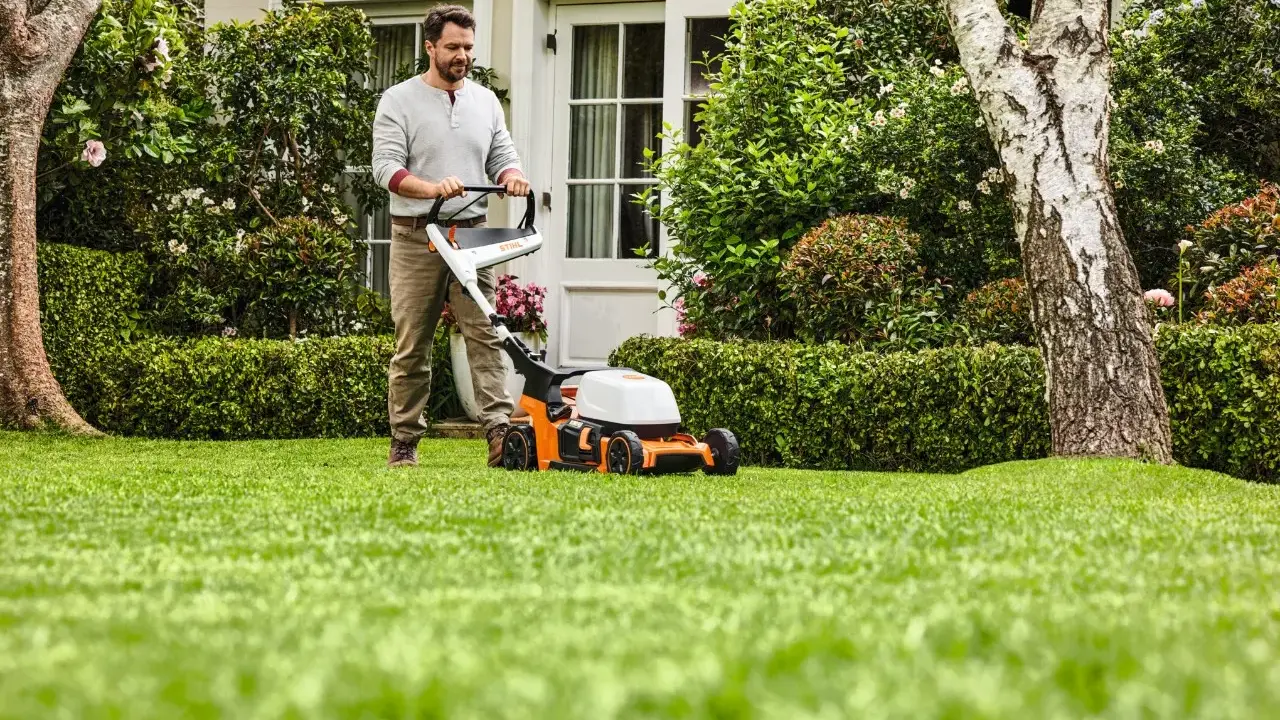 Homme tondant une pelouse verte avec une tondeuse STIHL orange et blanche.