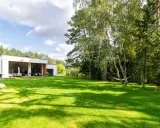 Maison moderne avec pelouse verte luxuriante et arbres, sous un ciel bleu nuageux.