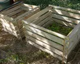 Deux composteurs maison en bois, l'un rempli de verdure, prêts à transformer les déchets de jardin en or noir.