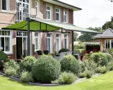 Aménagement terrasse devant maison avec auvent vert rayé, mobilier de jardin et végétation luxuriante.