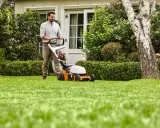 Homme tondant une pelouse verte avec une tondeuse STIHL orange et blanche.