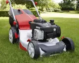 Tondeuse à gazon rouge et argentée sur herbe verte. Aide à choisir quelle tondeuse choisir pour un jardin impeccable.