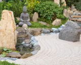 Jardin zen avec statue de Bouddha, cascade, étang et sable ratissé. Une allée de jardin facile à faire pour un coin de sérénité.