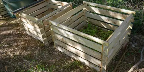 Deux composteurs maison en bois, l'un rempli de verdure, prêts à transformer les déchets de jardin en or noir.