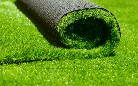 Rouleau de gazon synthétique vert vif, montrant le dessous noir et le dessus en fibres.