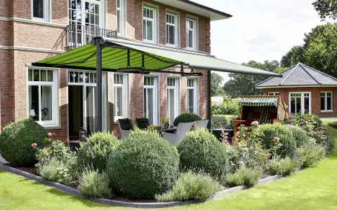 Aménagement terrasse devant maison avec auvent vert rayé, mobilier de jardin et végétation luxuriante.
