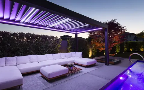 Pergola moderne avec éclairage LED violet, salon extérieur confortable, piscine illuminée. Une idée éclairage pergola pour une ambiance féerique.