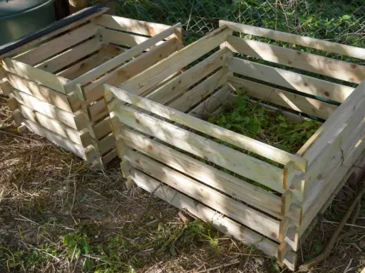 Deux composteurs maison en bois, l'un rempli de verdure, prêts à transformer les déchets de jardin en or noir.