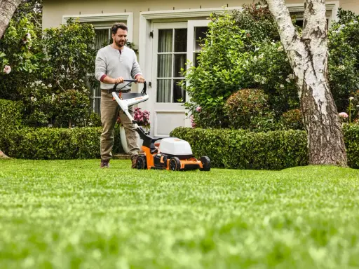 Homme tondant une pelouse verte avec une tondeuse STIHL orange et blanche.
