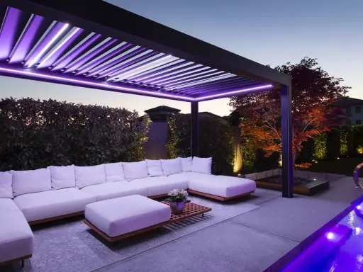 Pergola moderne avec éclairage LED violet, salon extérieur confortable, piscine illuminée. Une idée éclairage pergola pour une ambiance féerique.