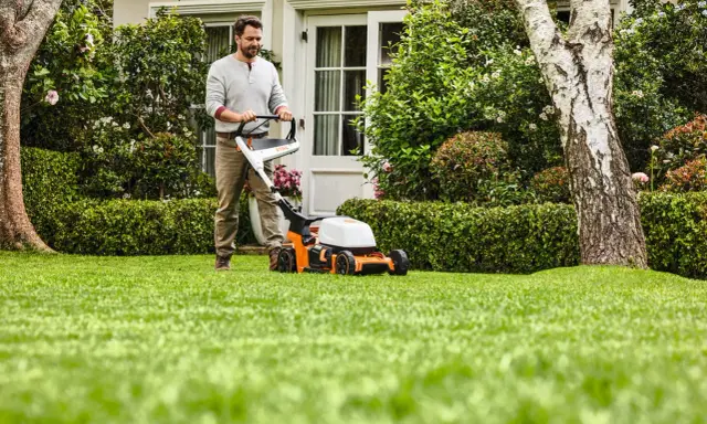 Homme tondant une pelouse verte avec une tondeuse STIHL orange et blanche.