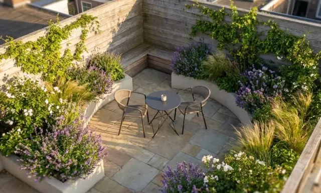 Idéal pour aménager un petit jardin de 10m2 : terrasse en pierre, banquette en bois, mobilier de jardin et massifs de lavande et graminées.