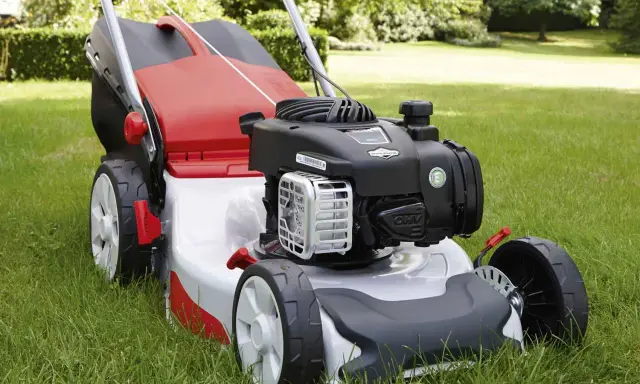 Tondeuse à gazon rouge et argentée sur herbe verte. Aide à choisir quelle tondeuse choisir pour un jardin impeccable.