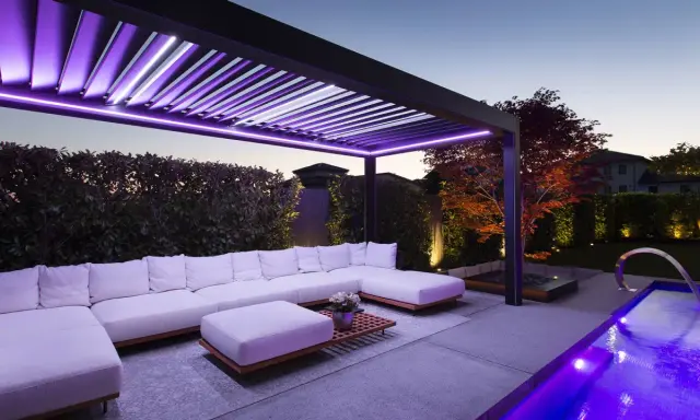 Pergola moderne avec éclairage LED violet, salon extérieur confortable, piscine illuminée. Une idée éclairage pergola pour une ambiance féerique.