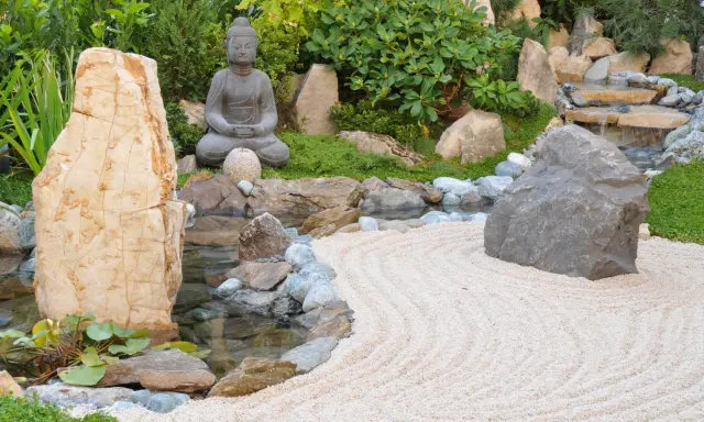 Jardin zen avec statue de Bouddha, cascade, étang et sable ratissé. Une allée de jardin facile à faire pour un coin de sérénité.