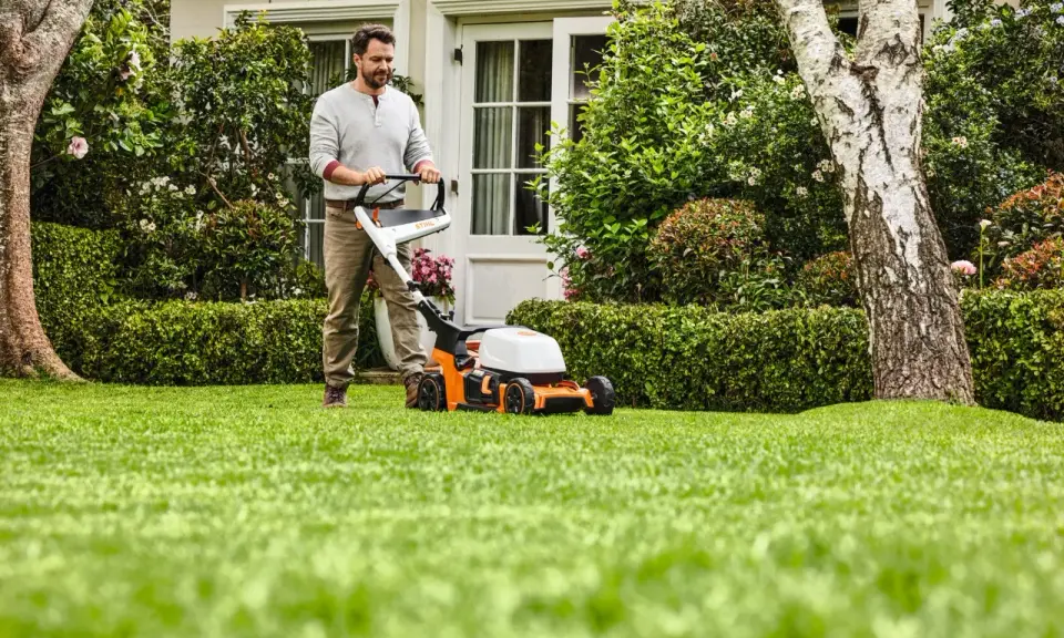 Homme tondant une pelouse verte avec une tondeuse STIHL orange et blanche.