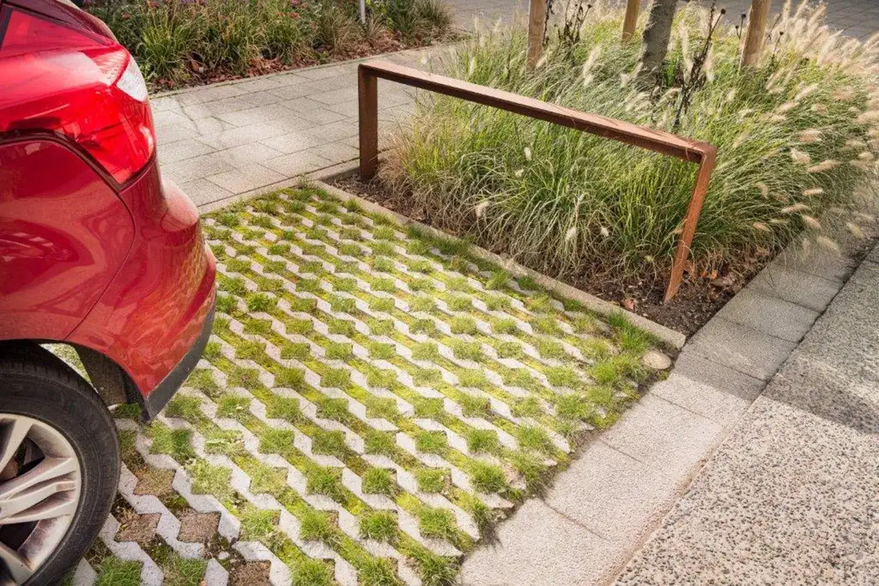 Une voiture rouge est garée sur une allée de garage drainante avec de l'herbe poussant entre les dalles.