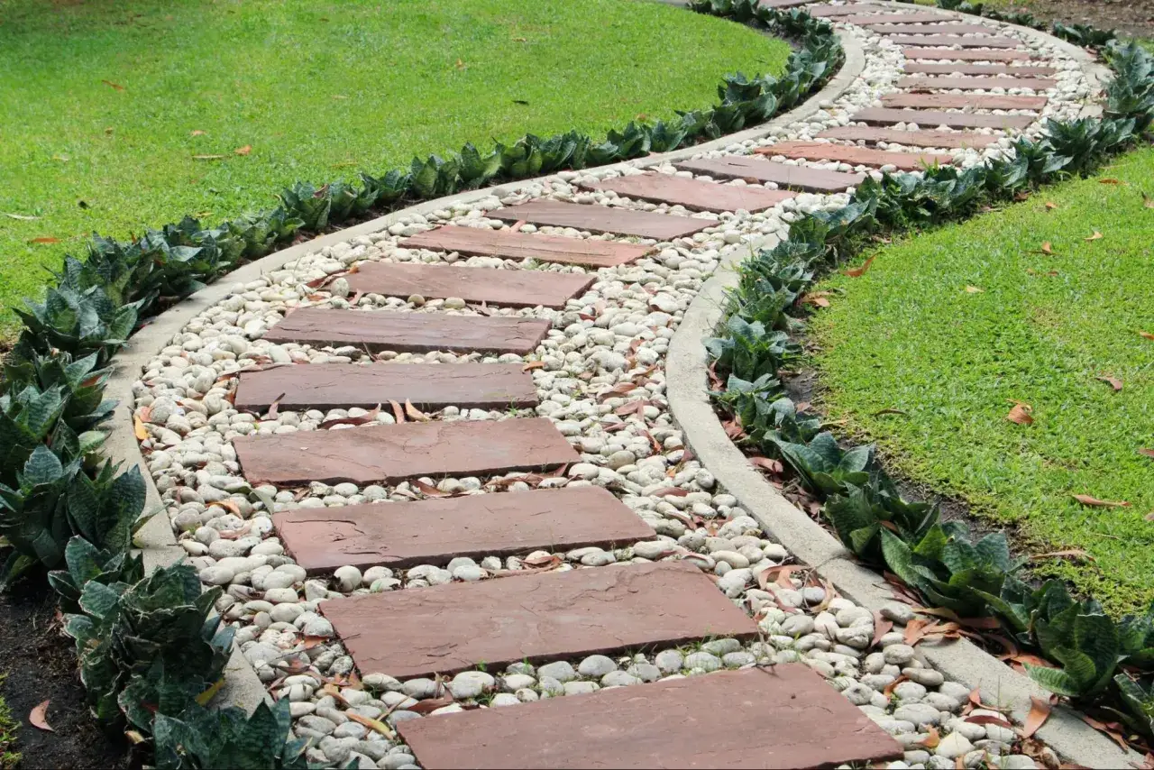 Une allée de jardin facile à faire avec des dalles de pierre rouge, des galets blancs et des plantes vertes luxuriantes.