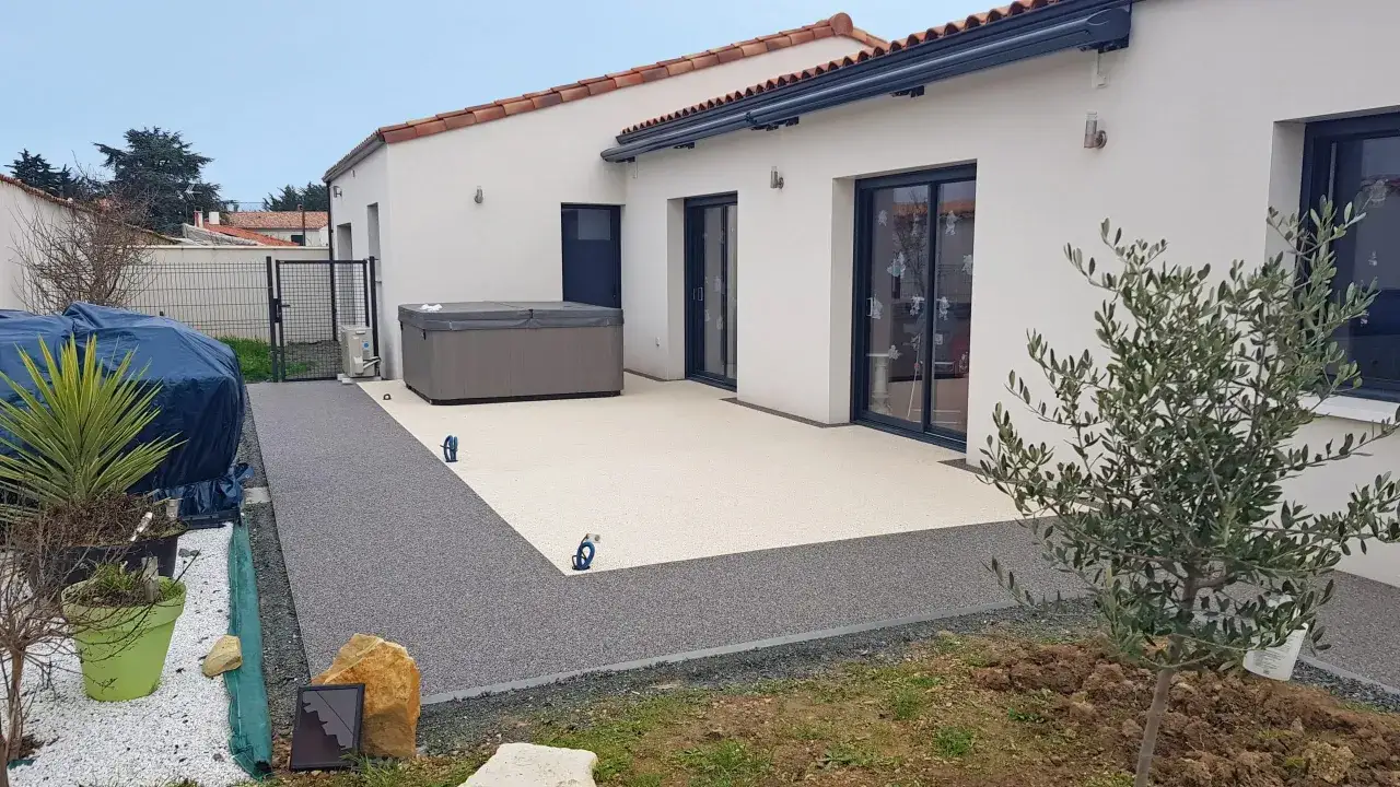 Aménagement extérieur sol : terrasse en résine claire et chemin en résine foncée, avec jacuzzi et olivier.