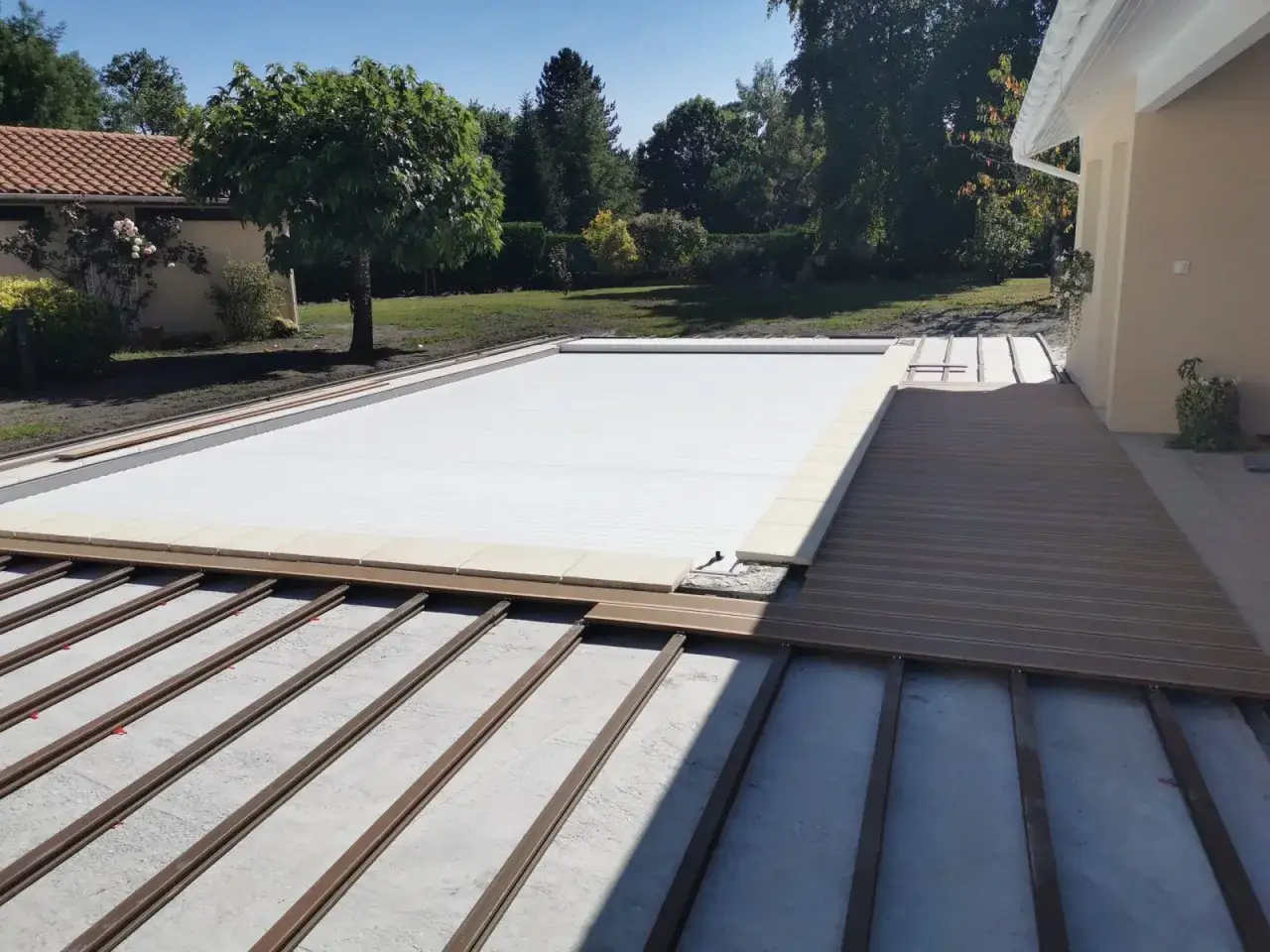 Construction d'une nouvelle terrasse en bois composite, en cours de refaire une terrasse sur une ancienne, à côté d'une piscine recouverte.
